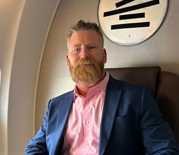 A businessman with a thick beard and stylish attire seated in a private jet, promoting luxury travel and professional success.