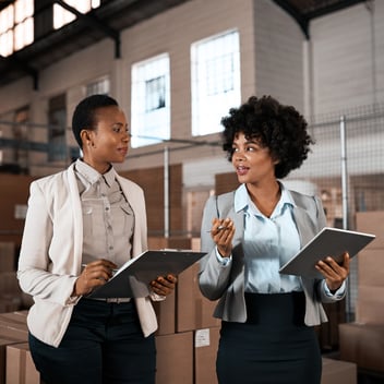 Two women having a discussion in a warehouse.