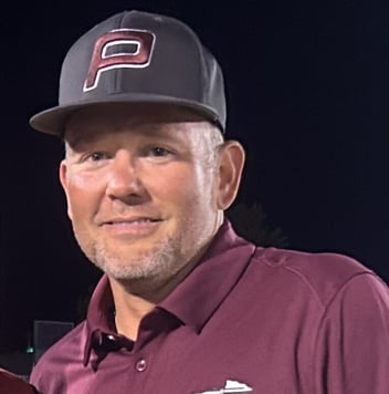 Portrait of a man wearing a gray cap and a maroon polo shirt, smiling in a nighttime outdoor setting.
