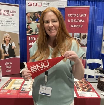 Woman smiling and holding a red SNU pennant at a booth showcasing Southern Nazarene University programs.