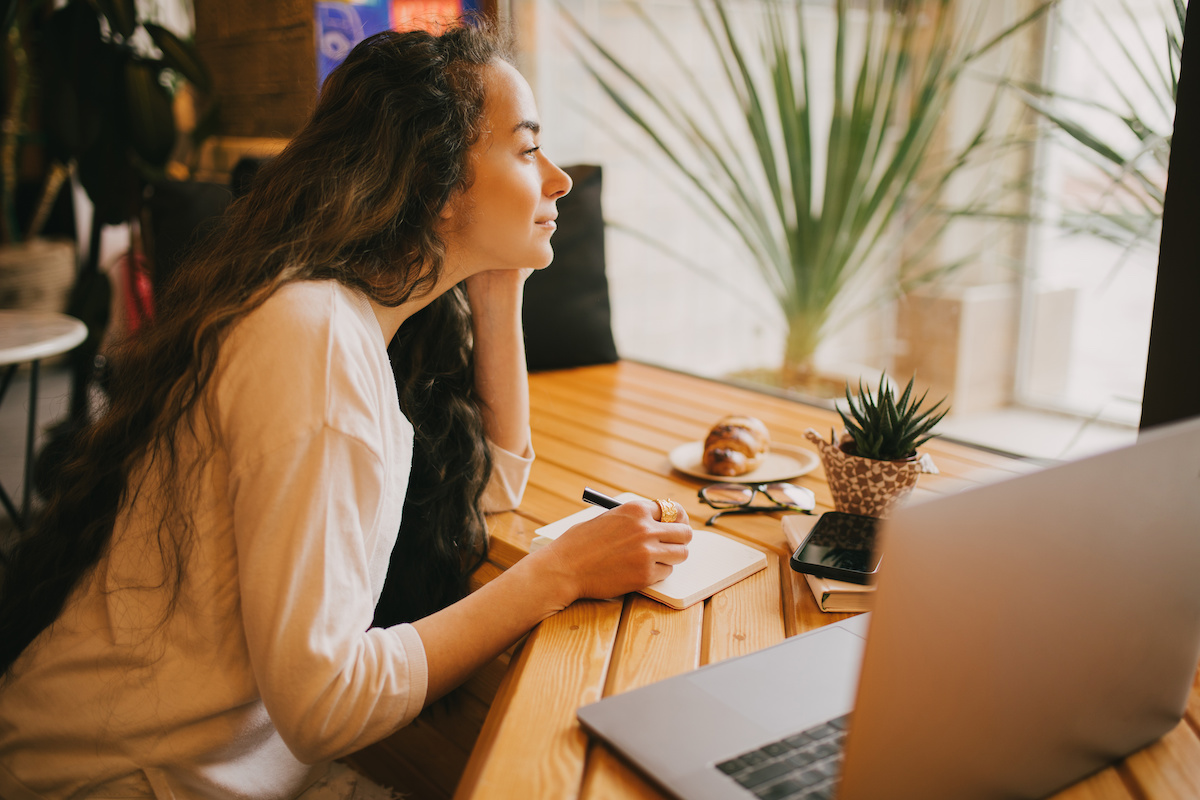 Young woman freelancer working online using her laptop, sitting in a coffee house and drinking coffee.