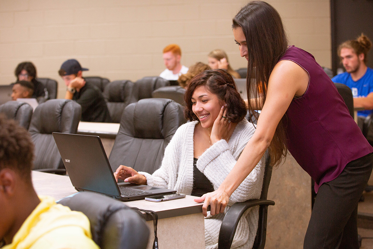 student working on computer with professor helping student