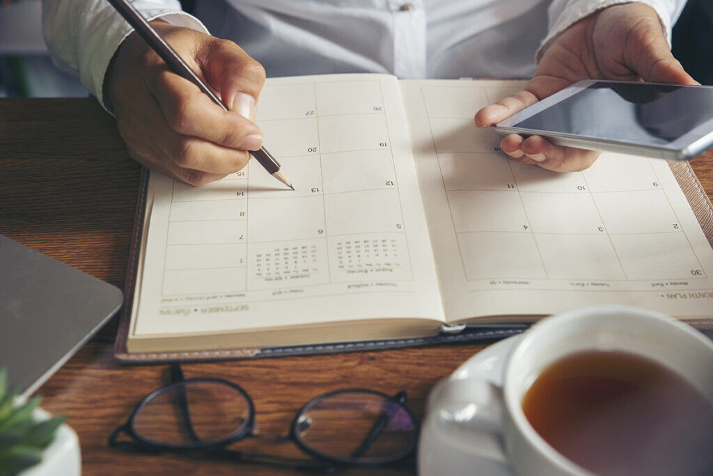 computer, hand writing in calendar, cup of coffee