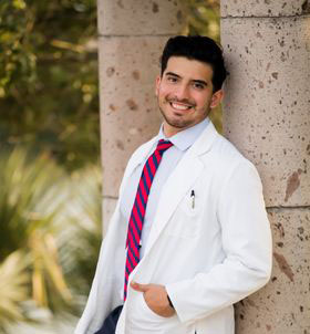 brandon perez wearing a doctors coat leaning against a pillar