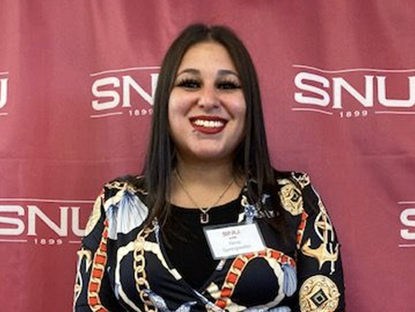 Nina Springwater standing, smiling, in front of SNU logo