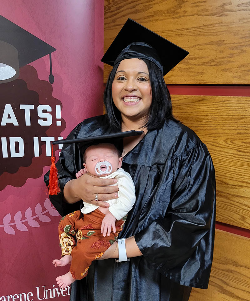 Jessica dressed in her graduation regalia holding her baby