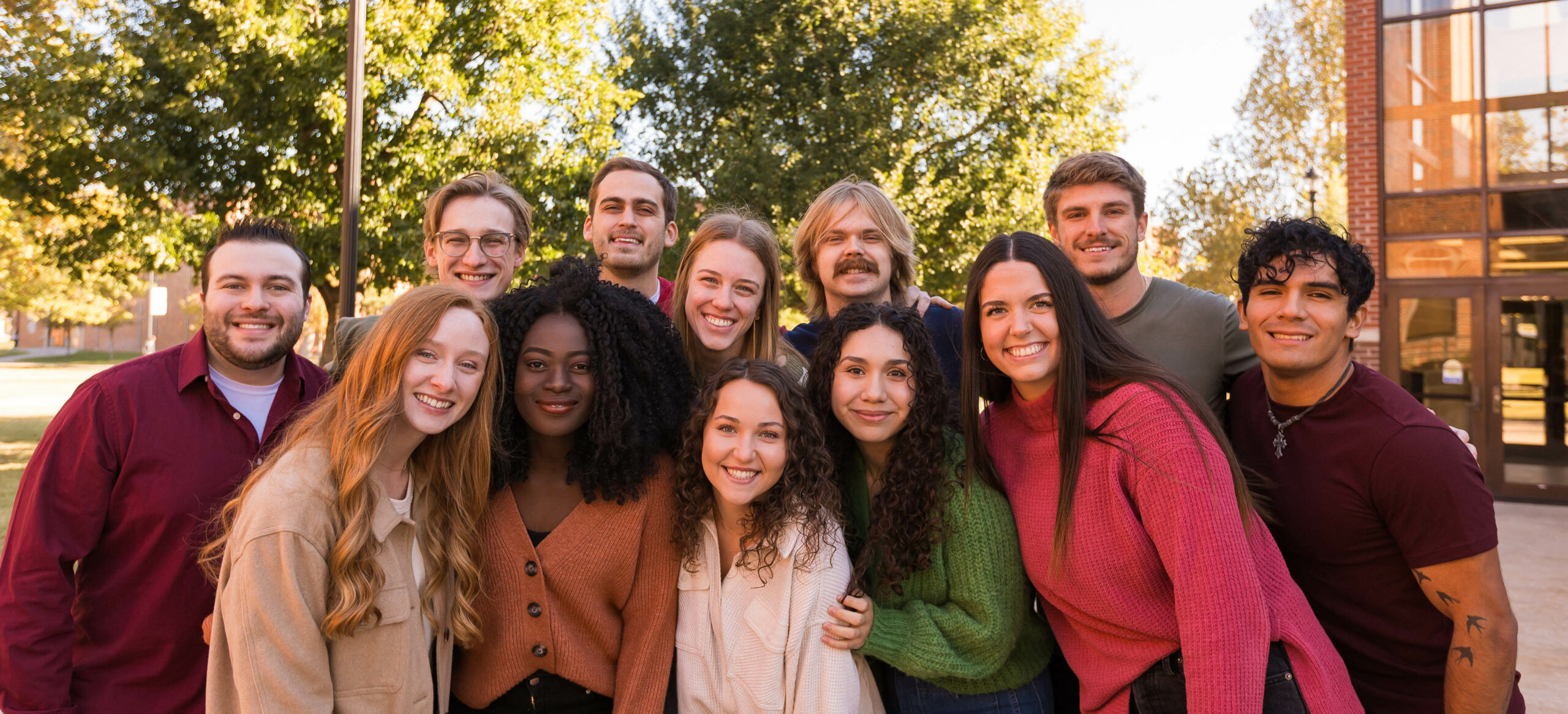 A diverse group of SNU students standing on the campus of SNU smiling, dressed in fall colors